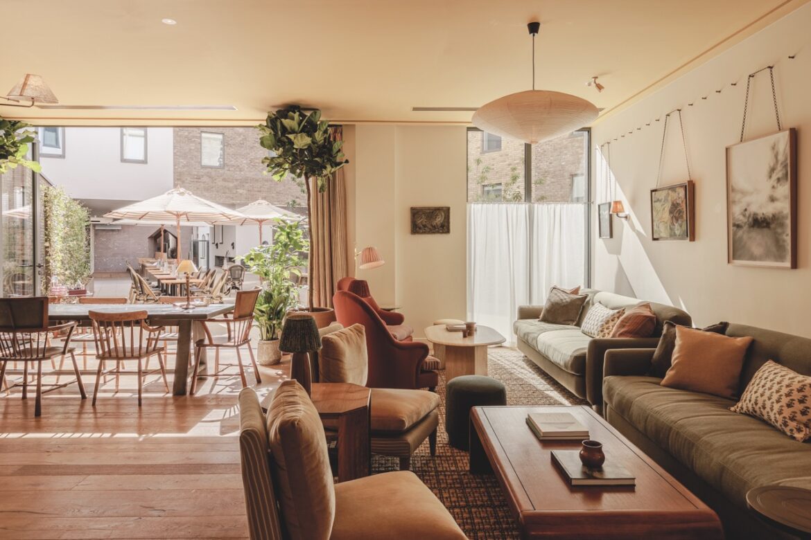 An open living room and dining room area with rows of couches and a large table. The doors are open to a garden area