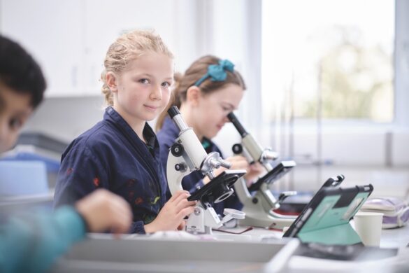 A classroom with a young girl looking at the camera with a microscope on the desk in front of her