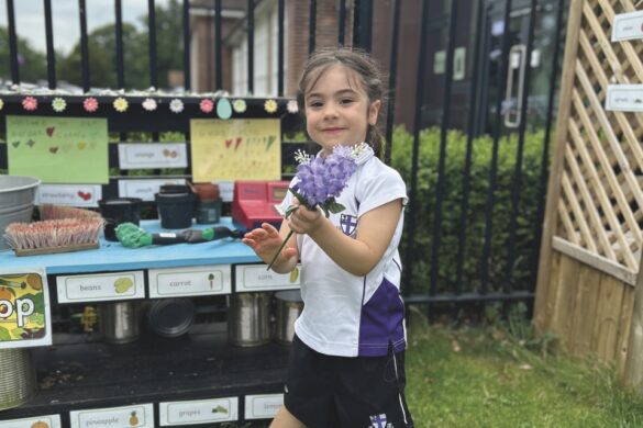 A young school child stands outside next to a marketstall and toys on the ground