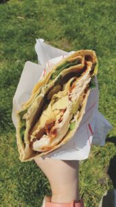 A breakfast wrap in white paper in front of green grass