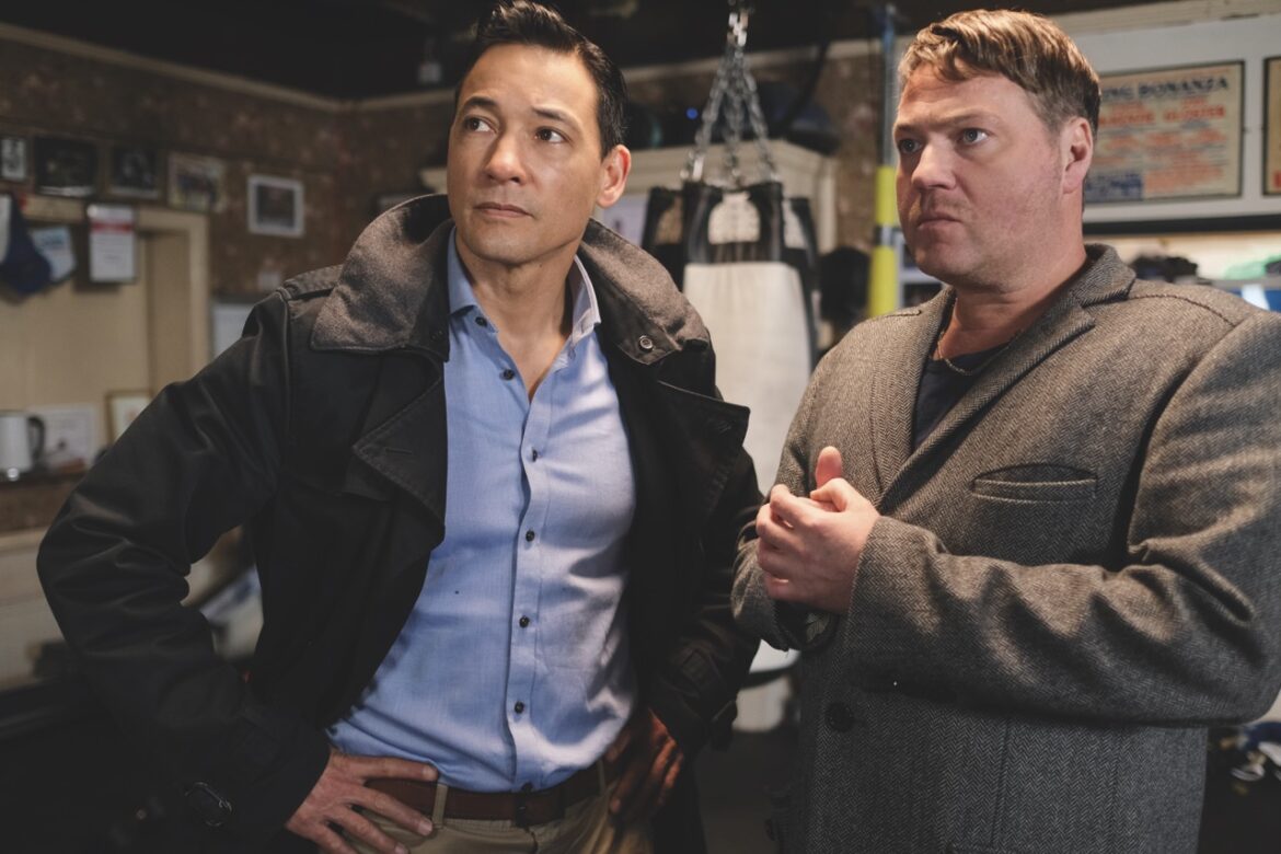 Two men stand next to each other in a boxing room with coats on
