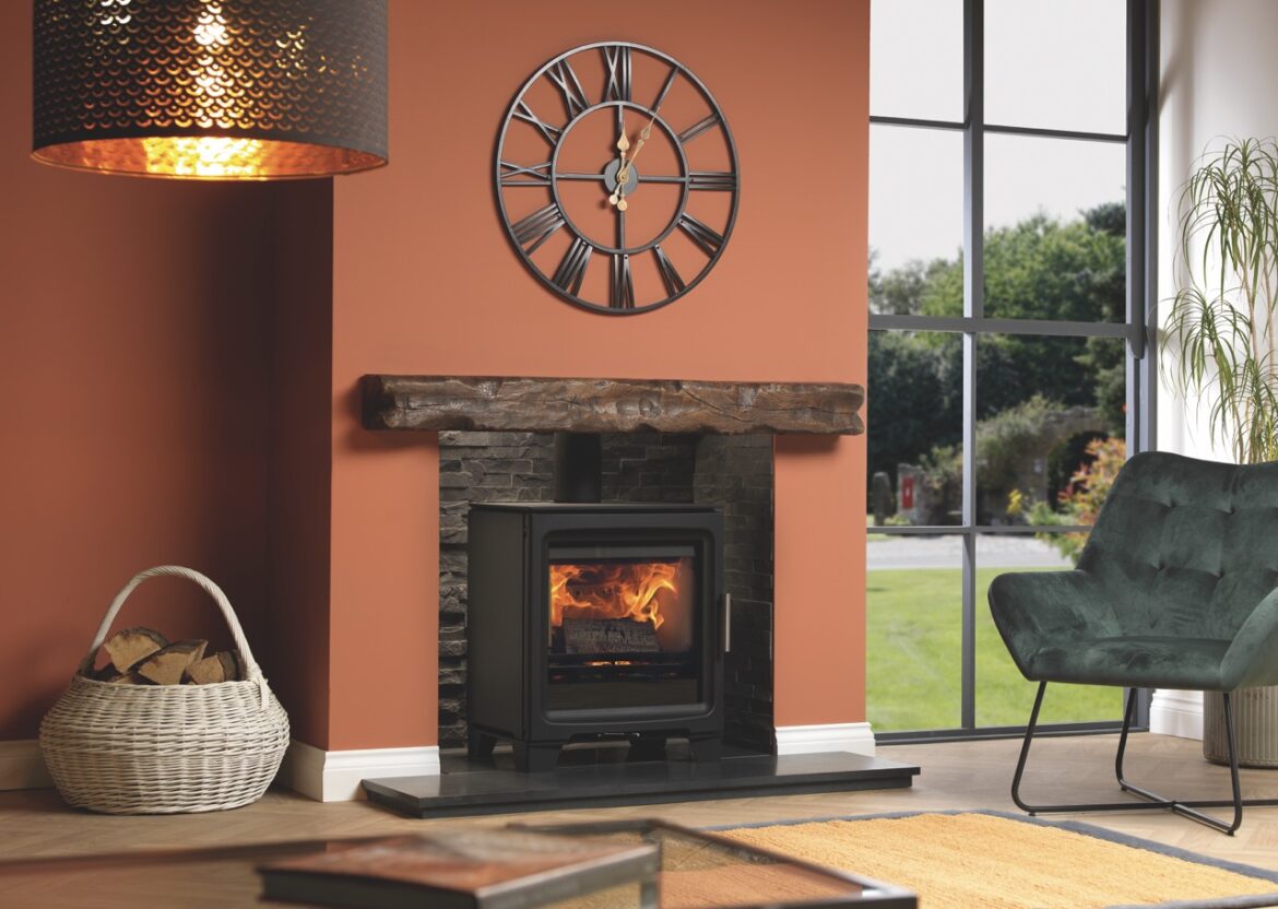 A living room with orange walls, a floor-length window and a black fireplace in the centre