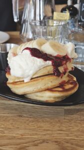 A stack of thick pancakes with cream, jam and bananas on top
