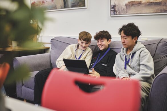 Three young boys work around a laptop while they sit on a sofa