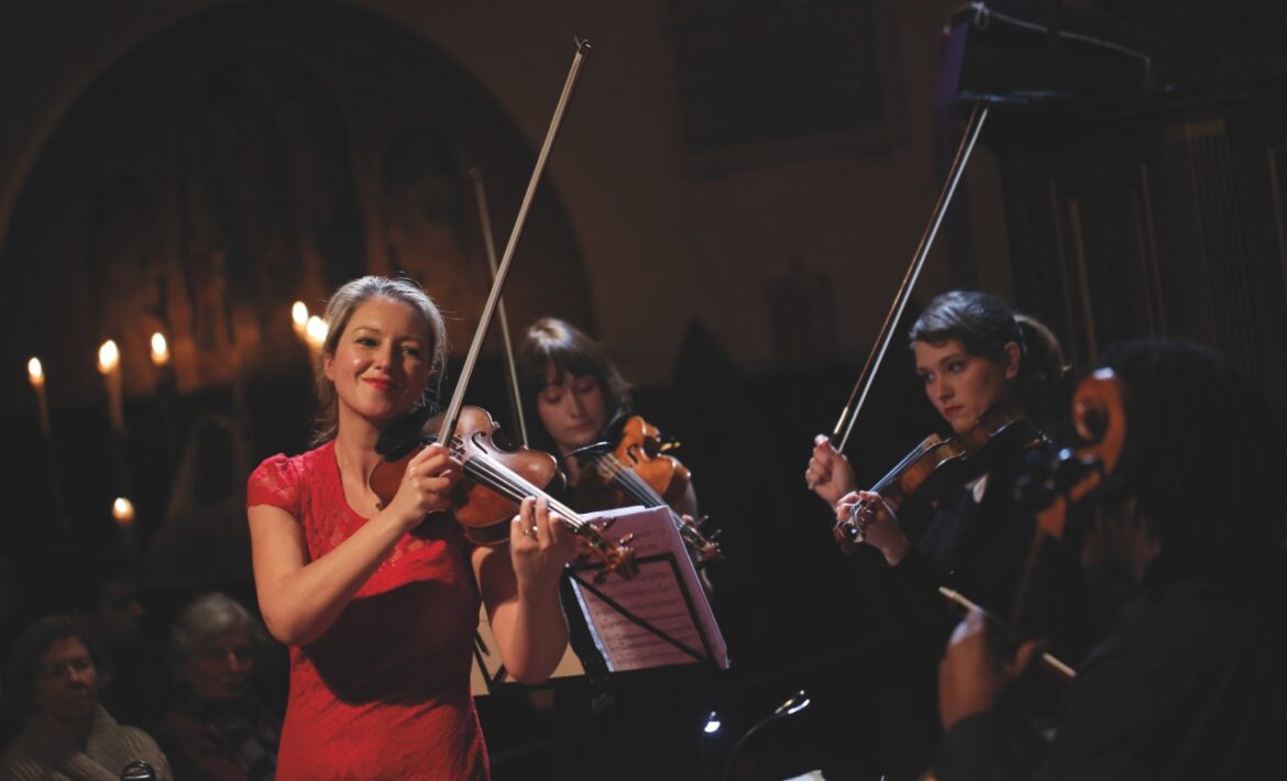 An orchestra on stage with a woman in red playing a violin in the foreground