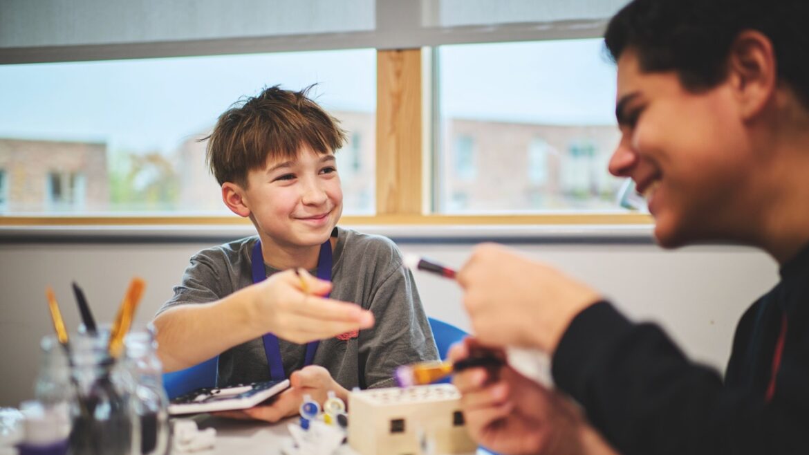 Two young boys sitting and laughing at a table in a classroom