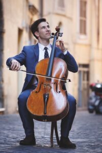 A man in a suit playing a cello in a street outside