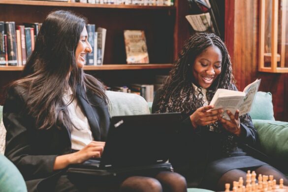 Two school girls sitting and working in a library on a couch