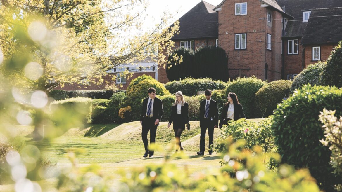 Four sixth form students walking through a field in front of a big house