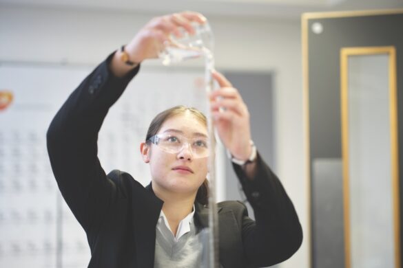 A school girl pouring a a chemical into a long tube while wearing safety goggles