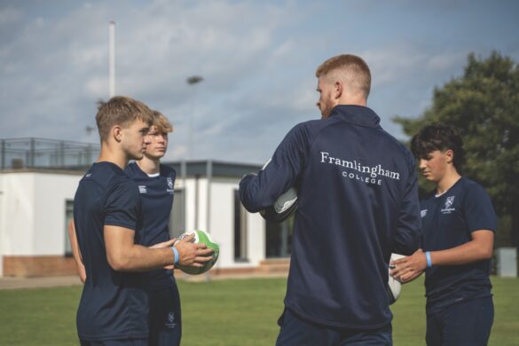 Three schools boys talking to a coach on a sports field at a school