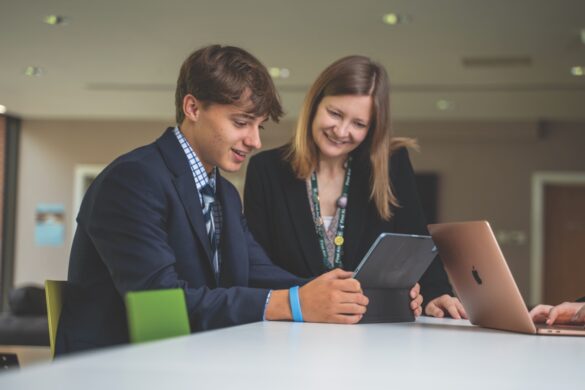 A teacher helping a school student as he works on a tablet at a table