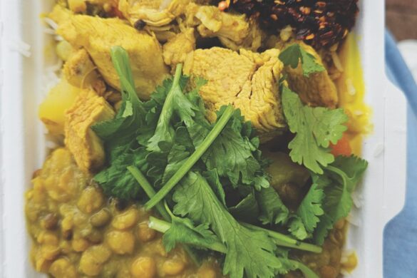 A curry with a yellow sauce in a takeaway box