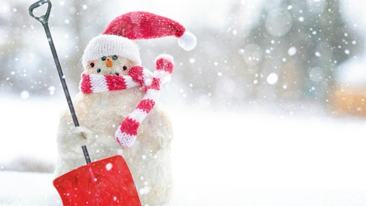 A snowman wearing a har and scarf and holding a red shovel in a snowy landscape