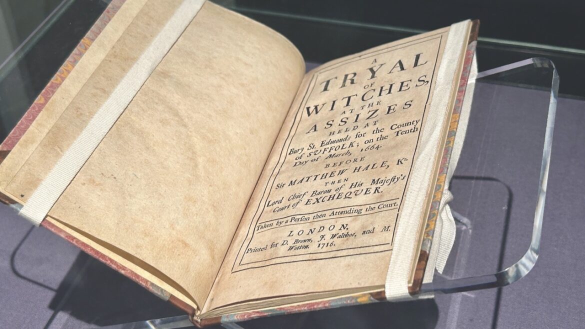 An old book about witch trials placed on a glass stand in a museum