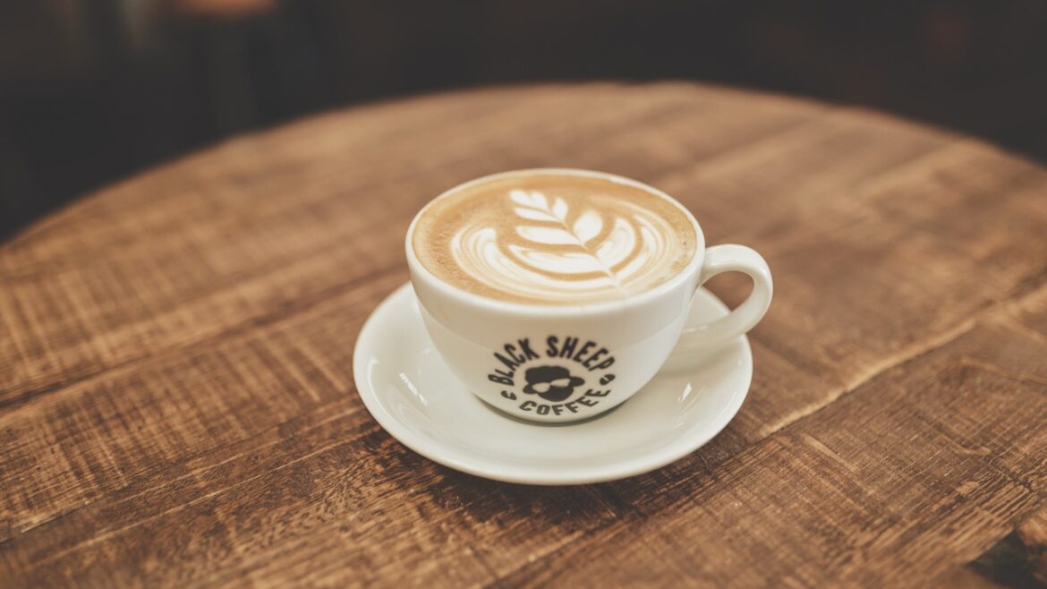 A coffee with foam art on the top sitting in a Black Sheep Coffee mug on a round wooden table