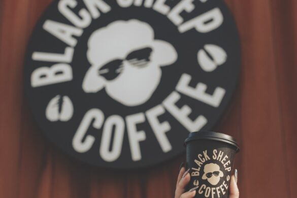 A hand holding a coffee cup up in front of a logo for Black Sheep Coffee