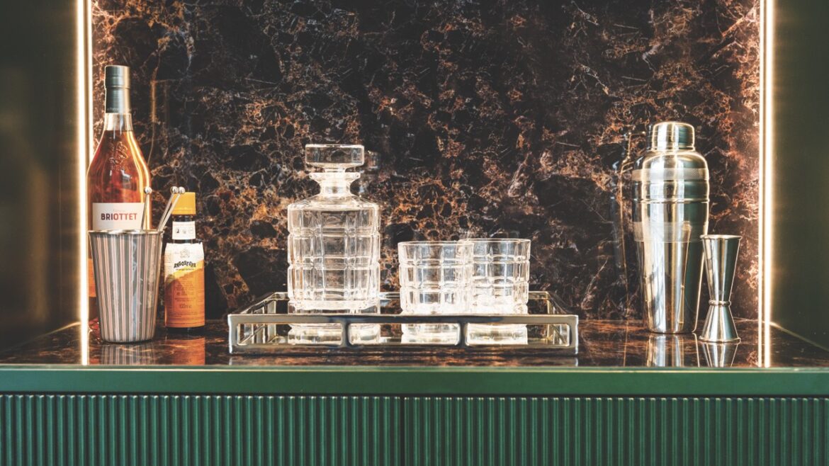 A home bar with glasses, alcohol and a cocktail shaker on a green surface