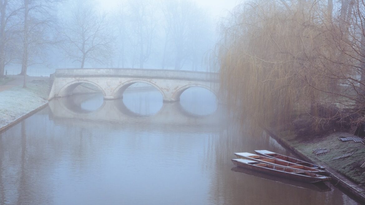A bridge over the River Cam on a foggy day with a punt moored nearby
