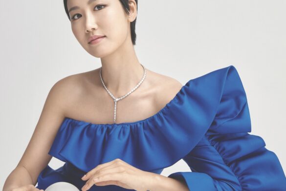 A woman wearing an elegant blue top and resting her hands on a crystal ball on a white table