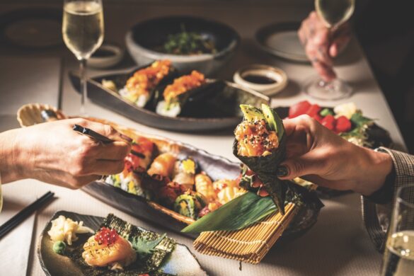 Sushi dishes with hands using chopsticks and holding a roll