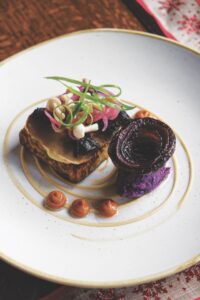 A mushroom toast dish on a white plate with a sauce circling the food