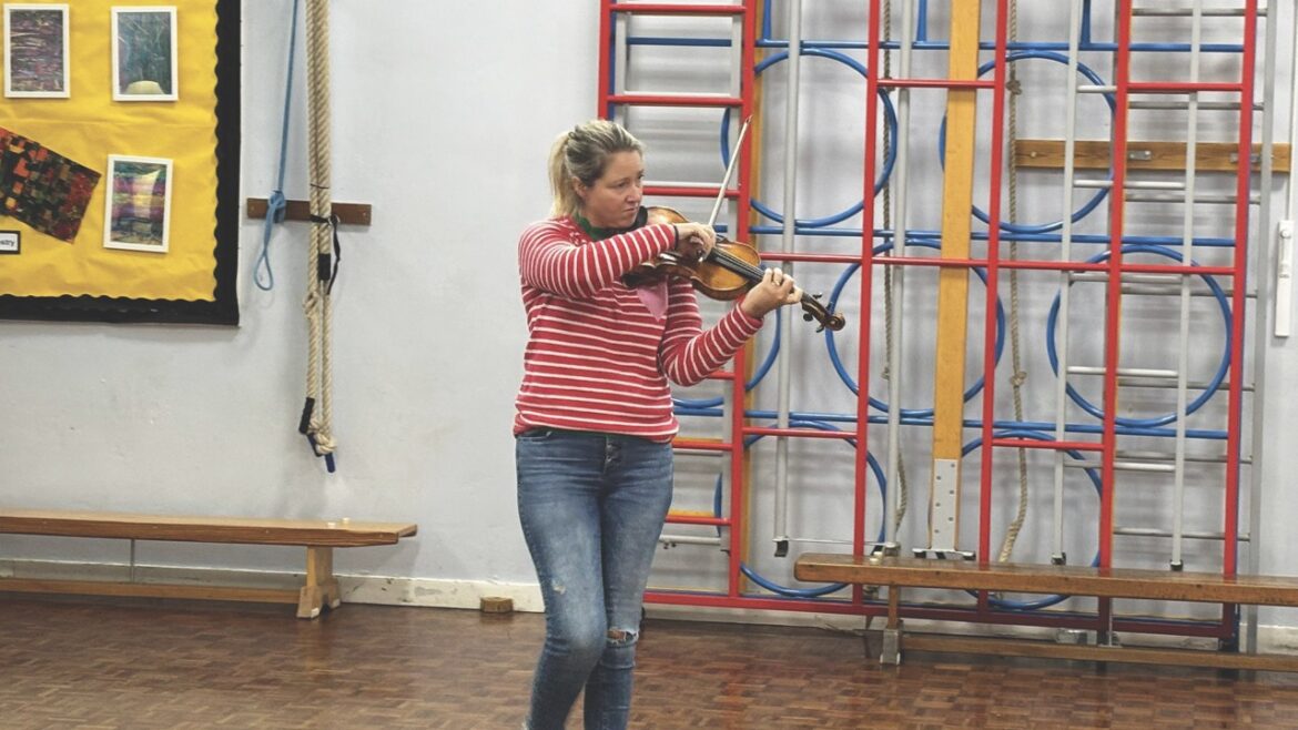 A woman standing in a school hall while playing violin