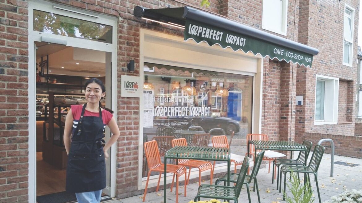 A young woman stands outside a new cafe with green and orange chairs outside