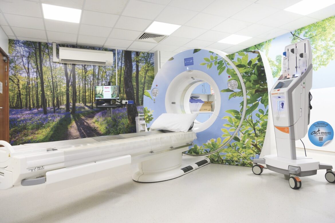 A CT machine in a medical room with a forest wall