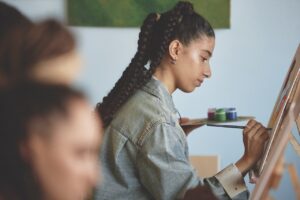 Young woman painting on canvas in an art studio, holding a palette and brush, focusing on creative process
