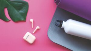 A leaf, yoga mat, water bottle and earbuds laying on a bright pink surface