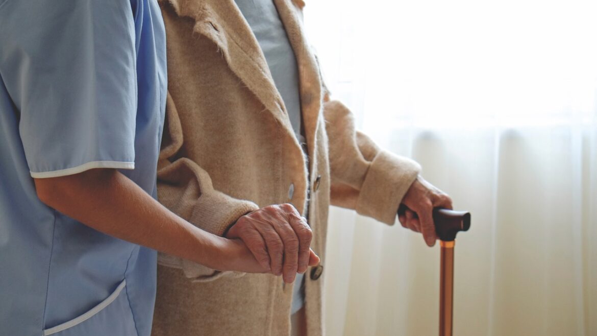 Hospital nurse taking care of mature female with walking stick in nursing home