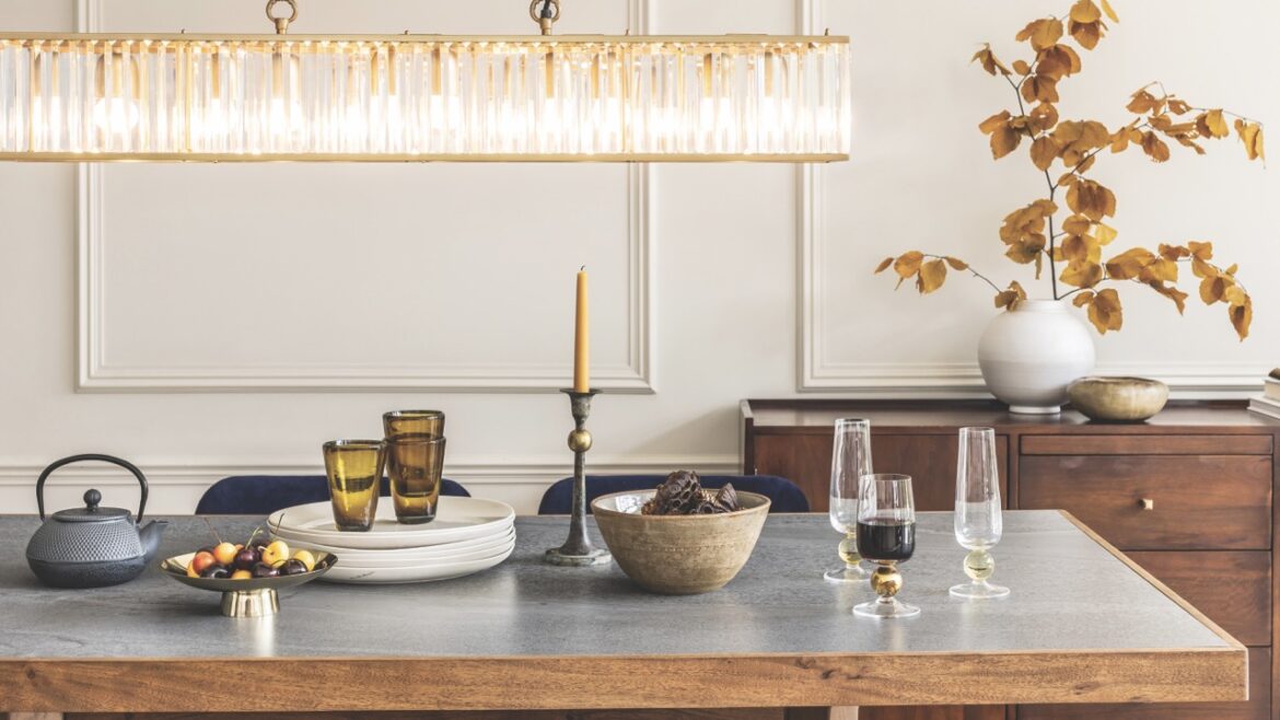 A large dining table with flatware and a large light hanging above