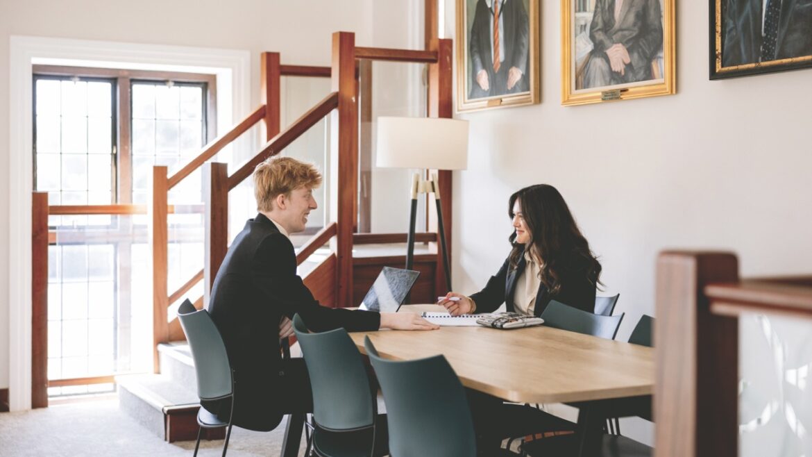Two young adults sit opposite each other at a table in a school