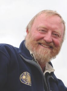 A smiling portrait of a man with a beard, standing outside