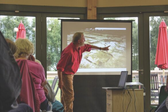 A man in a rd jumper points to a presentation on a screen
