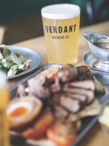 A pint of beer surrounded by blurred plates of food on a wooden table