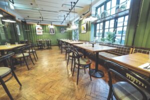 The empty interior of a restaurant with green walls and tables and chairs lining the room