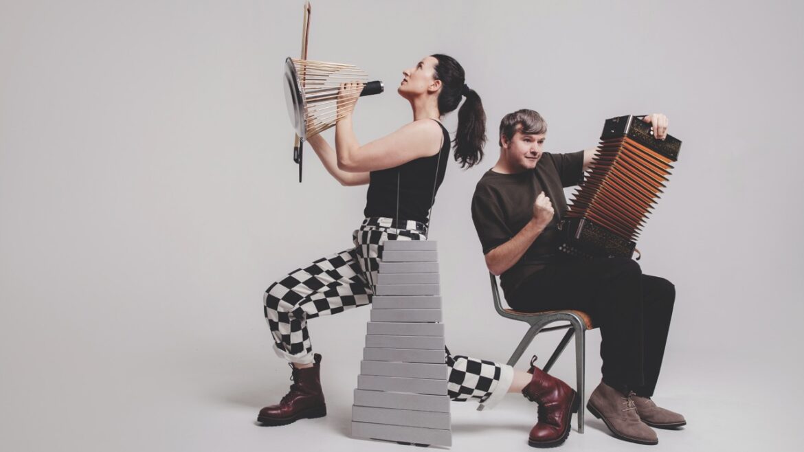 A woman lunging while playing numerous instruments and a man sitting on a chair while holding an accordion