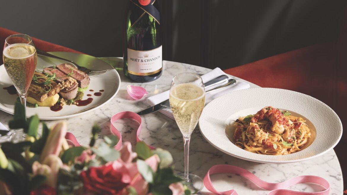 A table set up with pasta and steak alongside a glass of wine, pink ribbon and flowers
