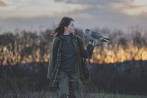 A woman walking in a field with a bird in their hand