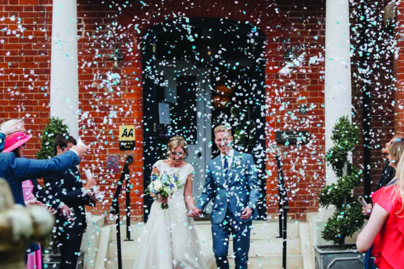 A bride and groom leaving a wedding venue as they are showered in confetti