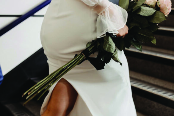 The legs of a person wearing a wedding dress and white shoes as they walk up some stairs, carrying a bouquet