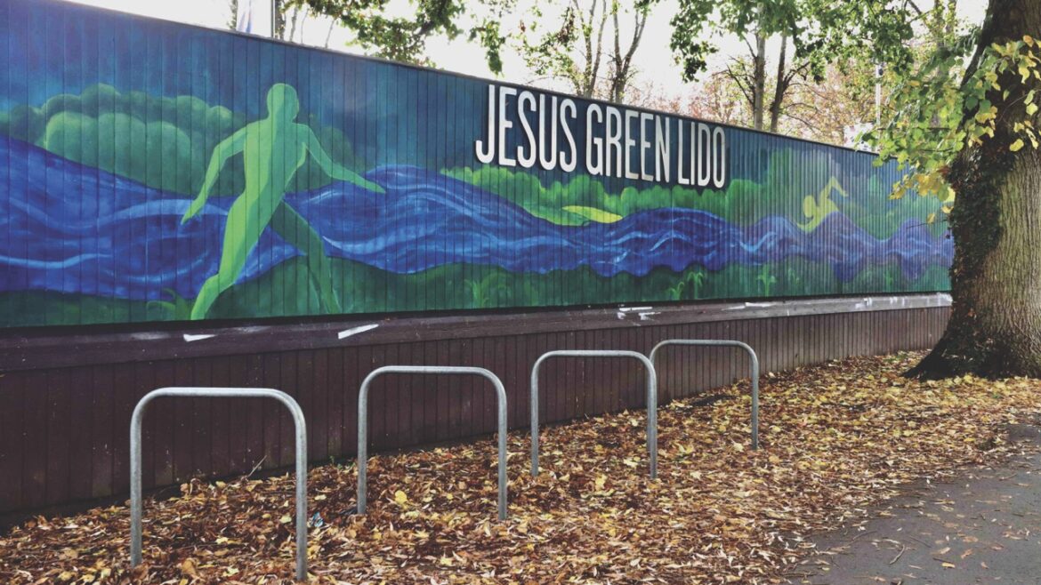 A swimming mural for Jesus Green Lido, behind bike racks and fallen leaves
