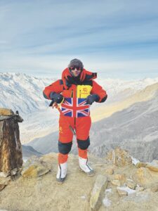 A person standing in a red snowsuit on the top of a mountain while holding a union jack