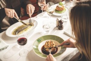 A group using their knives and forks to cut up the numerous dishes in front of them