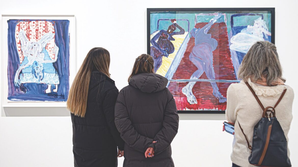 A group of three people with their backs to the camera as they look at artwork on a white wall