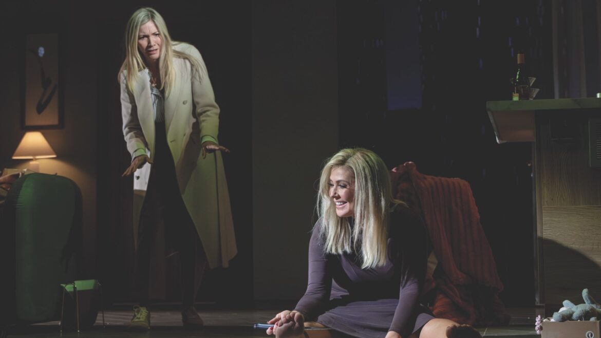 Two actors on a dark stage with one sitting on the ground in distress