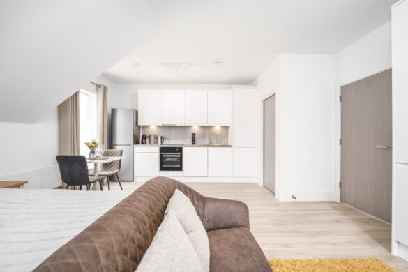 A modern living and kitchen area with white surfaces and a brown couch